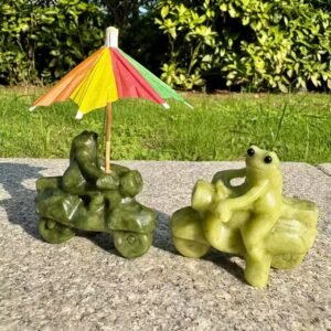 Two different handmade crystal frogs riding motorcycles, one light olive green and one deep forest green, posed with tiny colorful paper umbrellas.